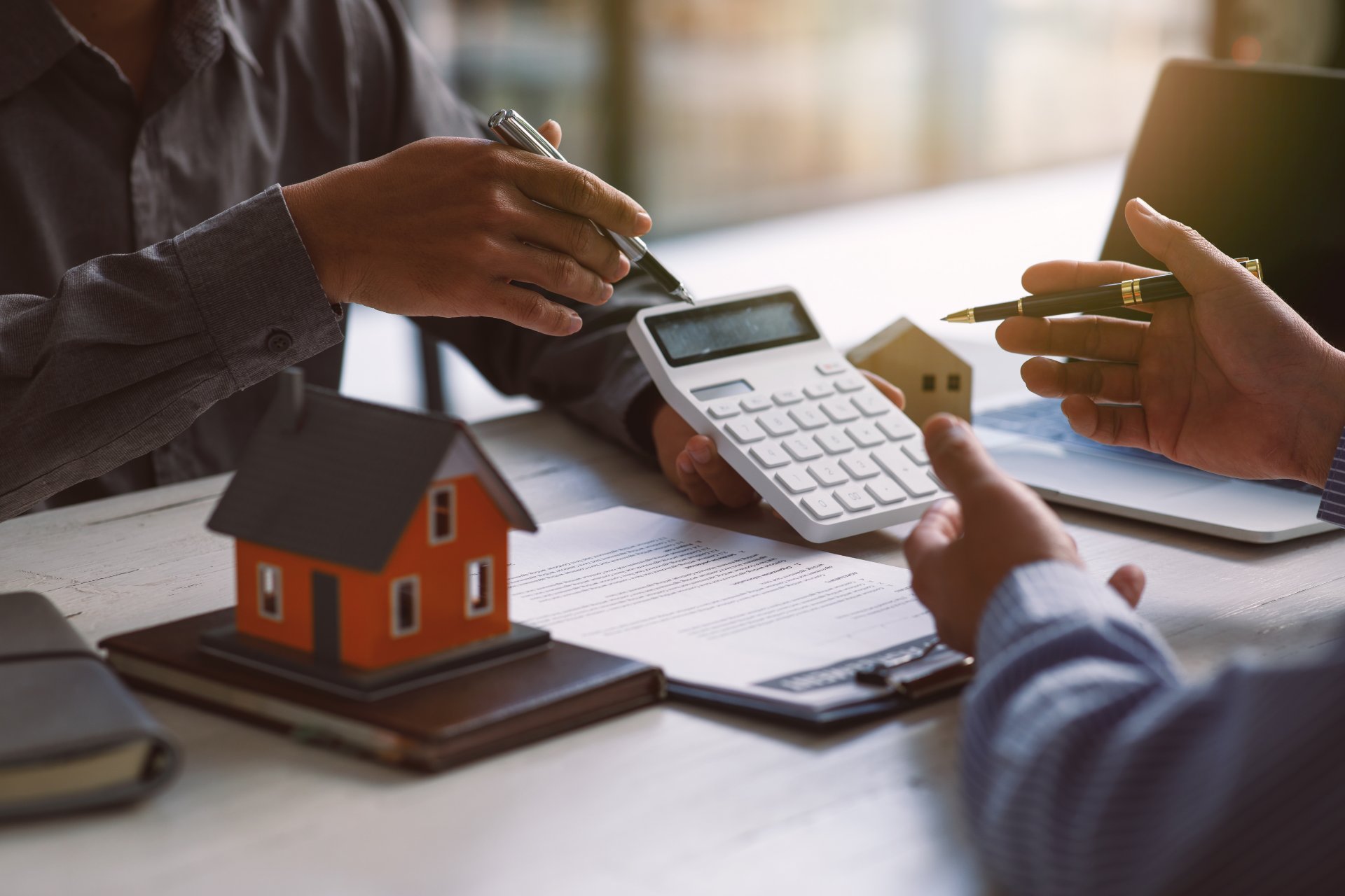 Hombre muestra una calculadora a otra con documentos y maquetas de casas sobre la mesa